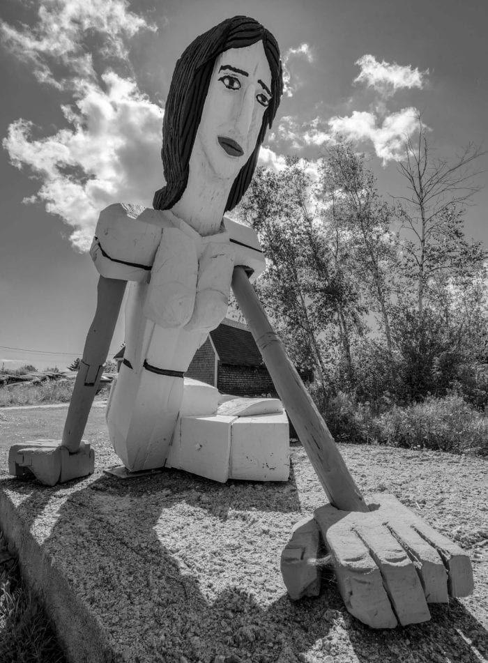 A large wooden sculpture that looks like Christina Olson in the famous painting Christina's World