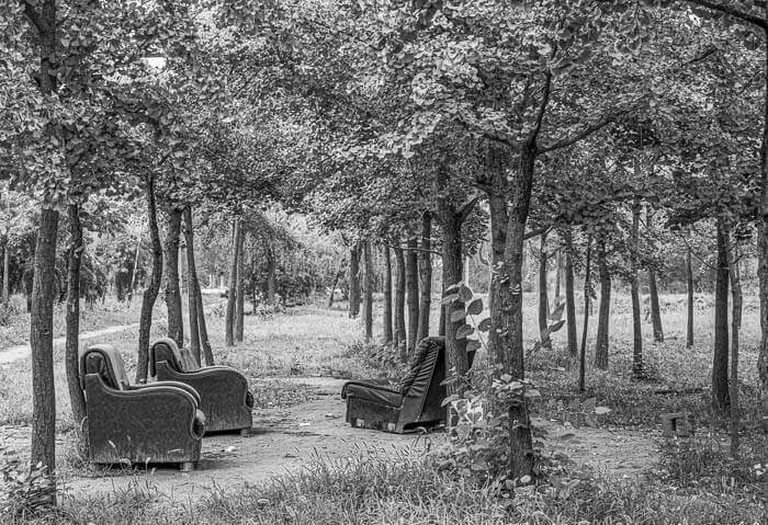 Three comfortable old chairs sit under trees in an open space in Beijing