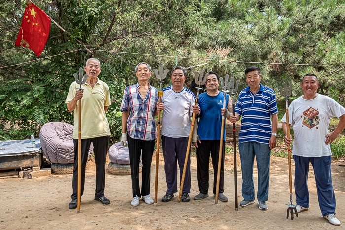 Six men stand holding thier martial art spears in the park.